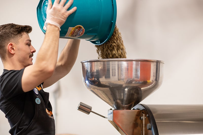 Nick pouring a bucket of coffee beans into the roaster at Union Place Coffee Roasters