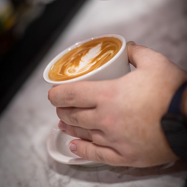 A cup of fresh brewed latte with a leaf drawn in the foam