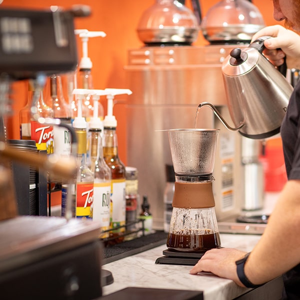 Employee pouring hot water over coffee grounds in a pour-over coffee maker