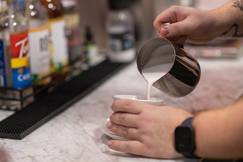 A barista's hands holding a cup and pouring milk into it