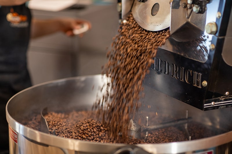 Commercial coffee roaster with roasted beans pouring into the stainless steel bucket